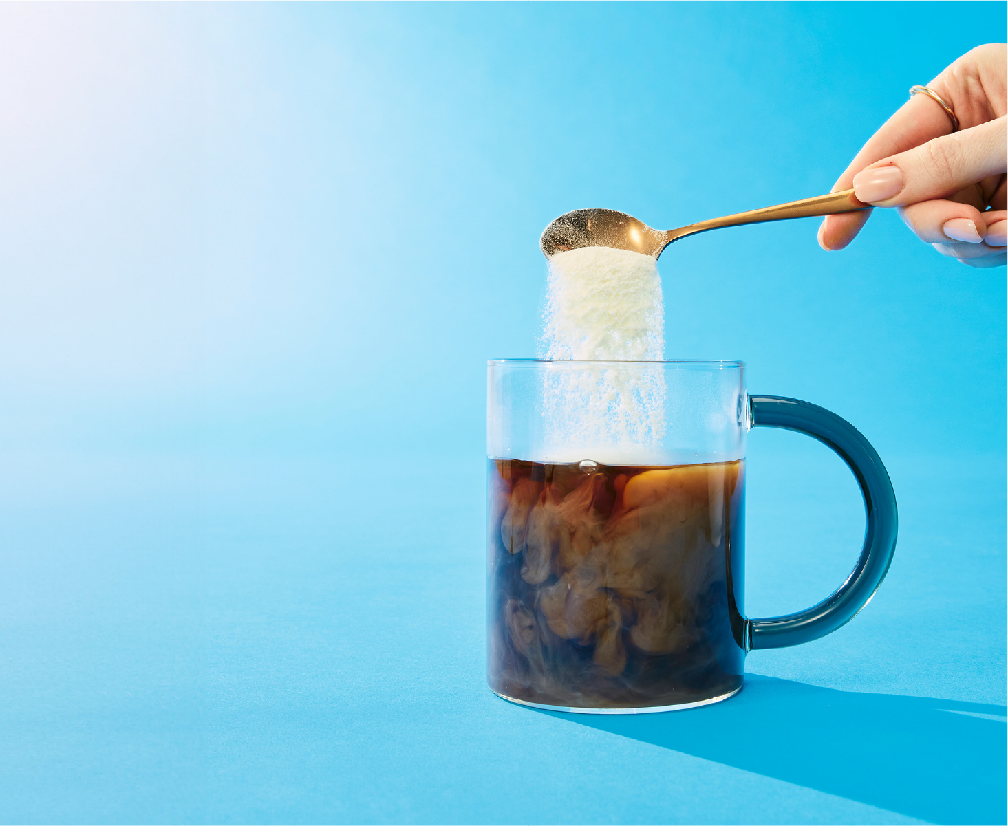  A golden spoon adding creamer powder into a cup of coffee